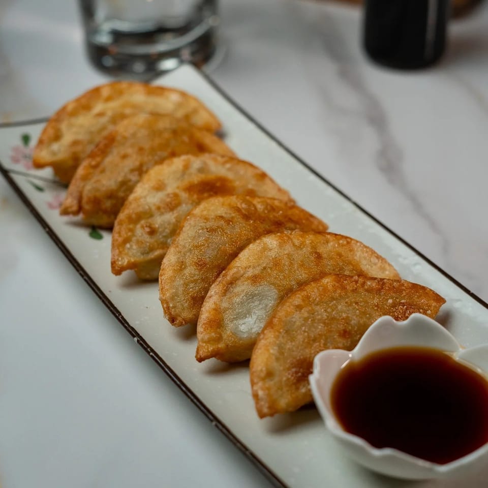 Crispy fried dumplings with a side of soy sauce on a white rectangular plate.